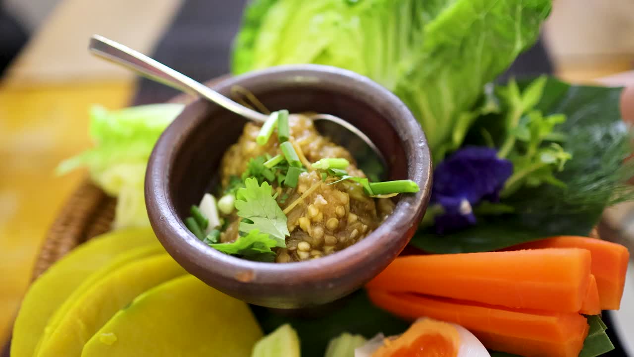 Close-up sequence of a rustic bamboo basket holding roasted green chili dip in a clay bowl, surrounded by colorful fresh vegetables, under soft natural lighting with gentle camera movement