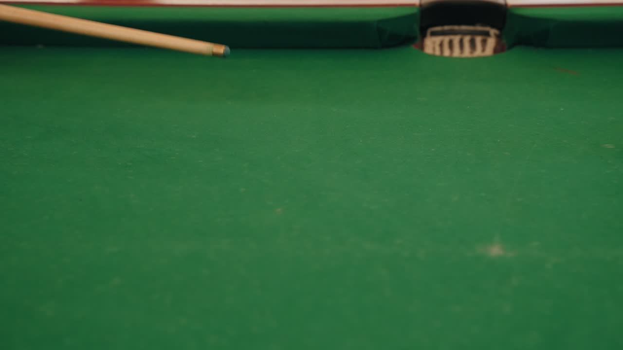 white cue ball approaching pocket on green billiard table with cue stick in frame