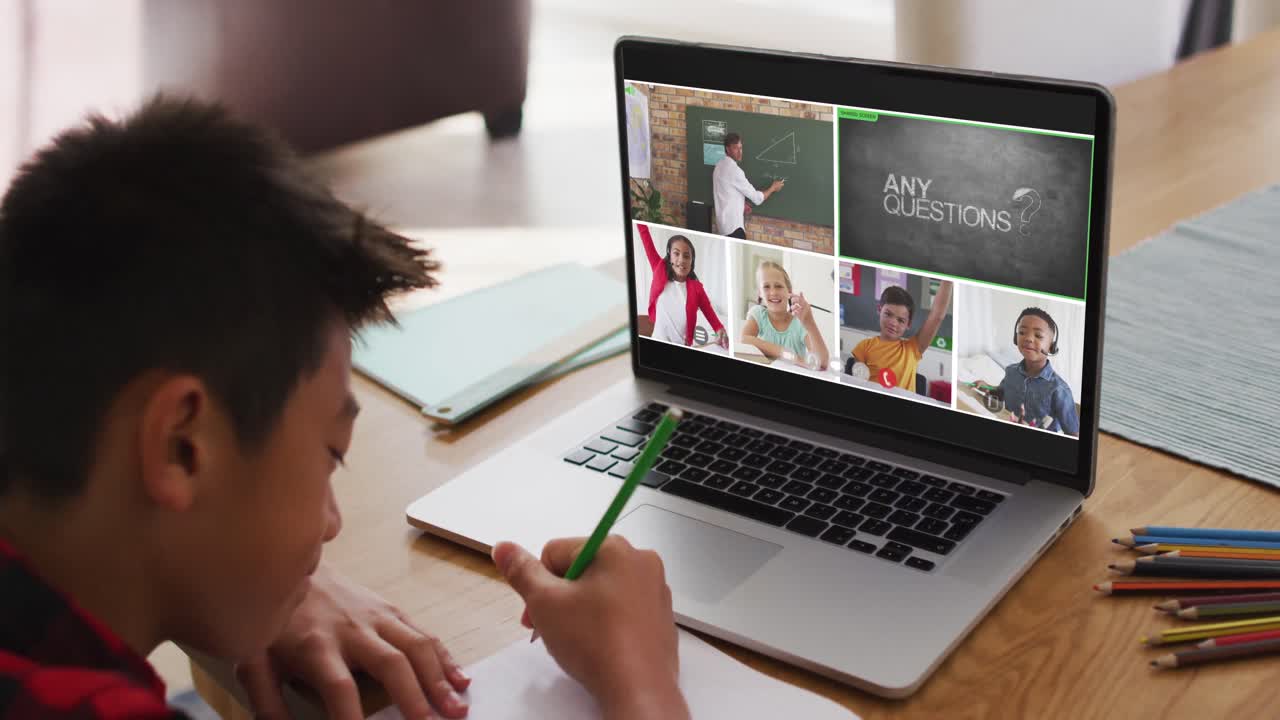 Schoolboy using laptop for online lesson at home, with diverse teacher and class on screen
