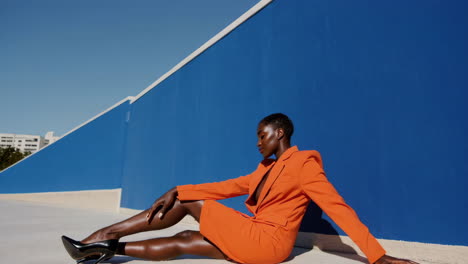 stylish woman in orange suit posing against a blue wall