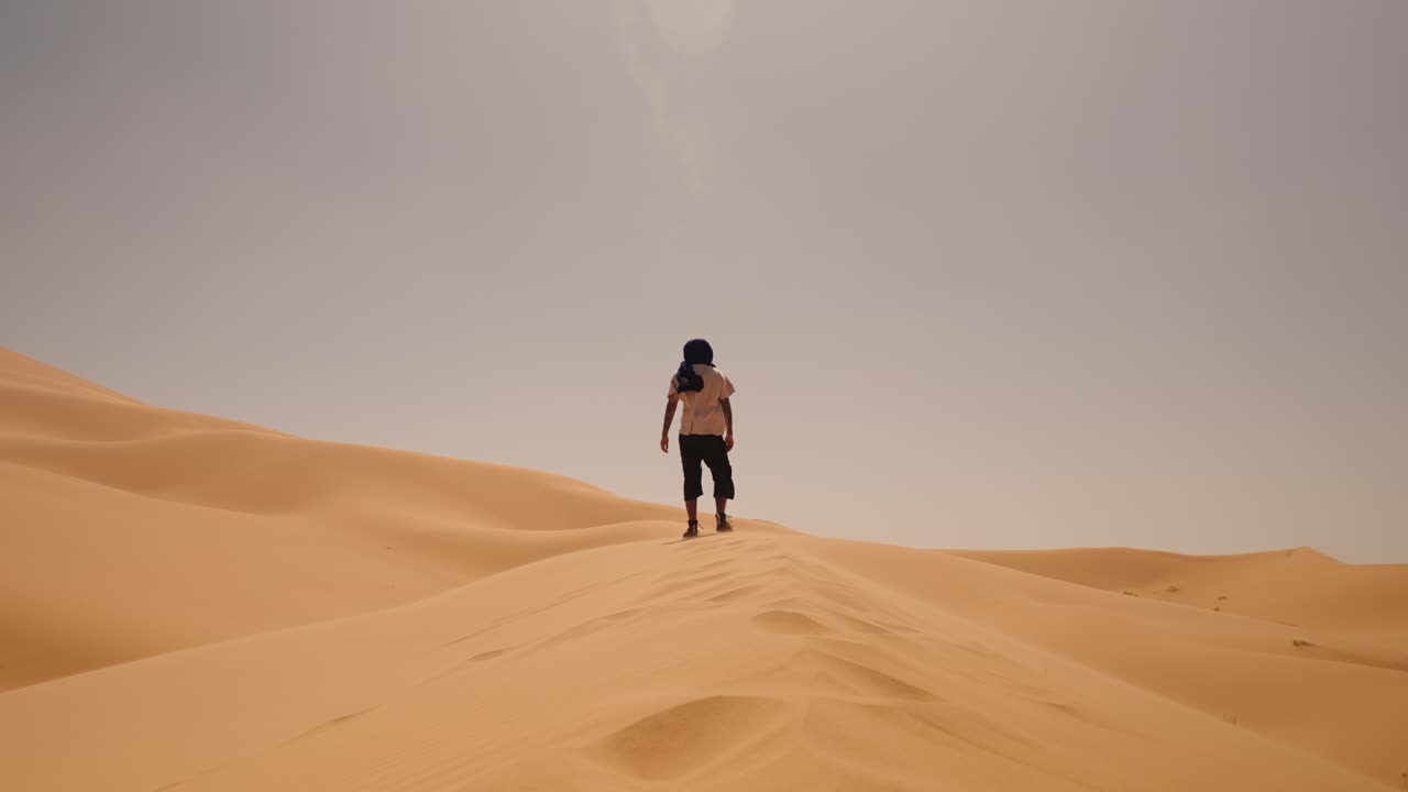 A lone traveler stands on Sahara dunes in Morocco, looking over golden sands
