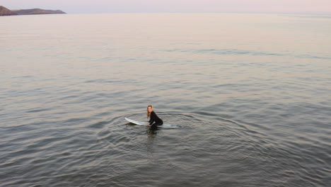 drone shot of woman wearing wetsuit paddling surfboard out to sea