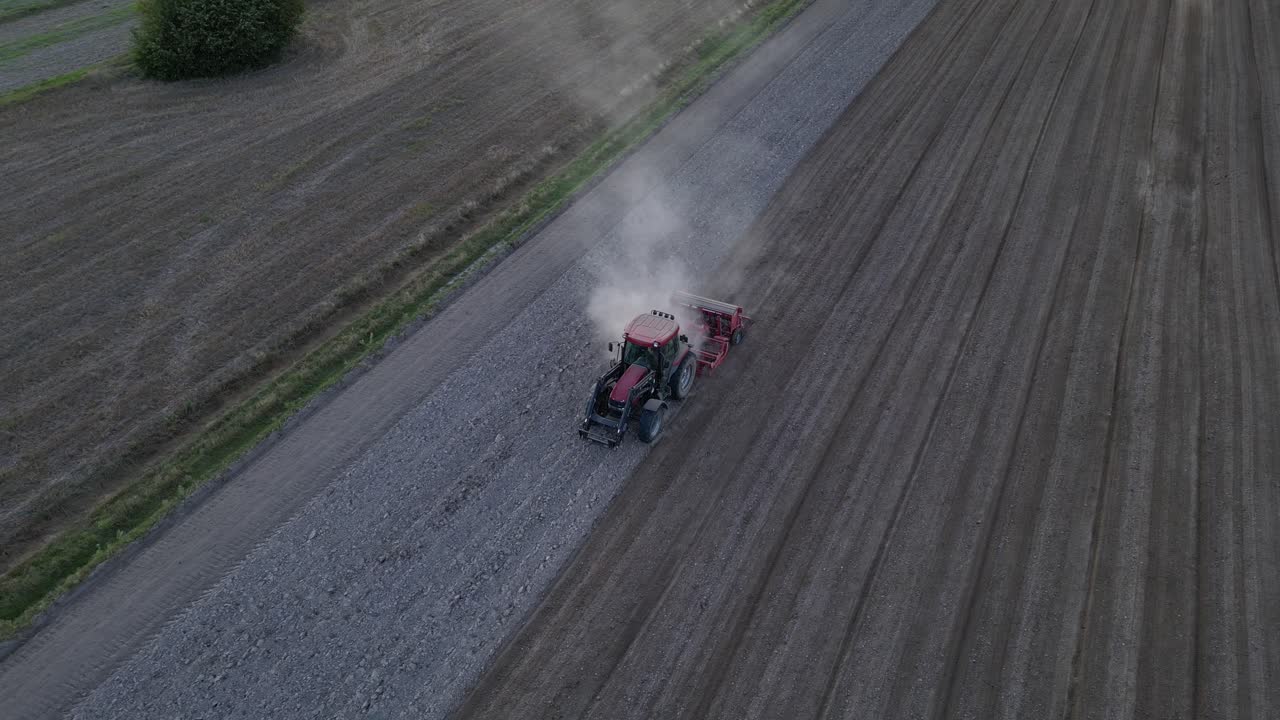 Drone footage of red tractor tilling dry soil with cultivator during autumn drought. Dust rises behind machine as it prepares land for winter