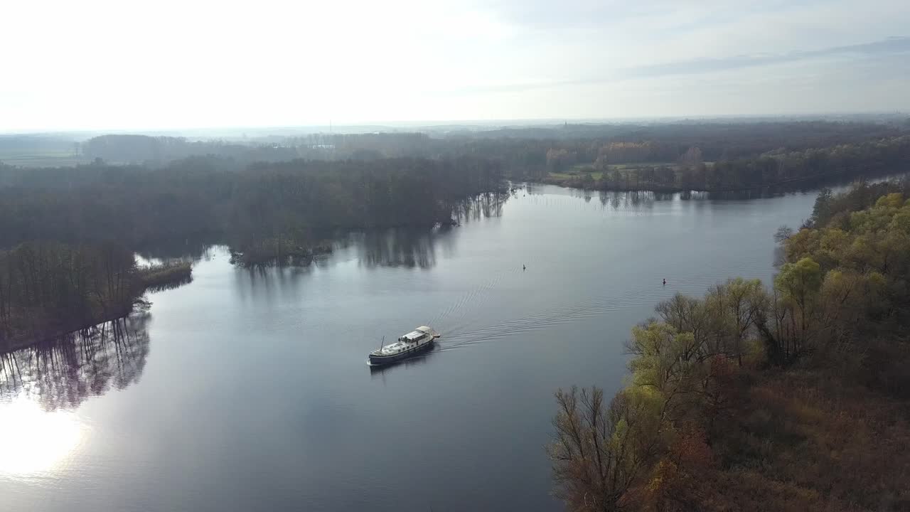 Ripresa aerea che segue un'imbarcazione che si muove lungo il fiume Elba (Labe), fiancheggiato da fogliame autunnale e acque calme e riflettenti.