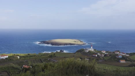 Vista-De-Drones-De-Un-Pueblo-Costero-Rural-Con-Un-Faro-Y-Una-Isla-En-El-Océano-Atlántico,-Cielo-Nublado-En-Topo,-Isla-De-São-Jorge,-Las-Azores,-Portugal