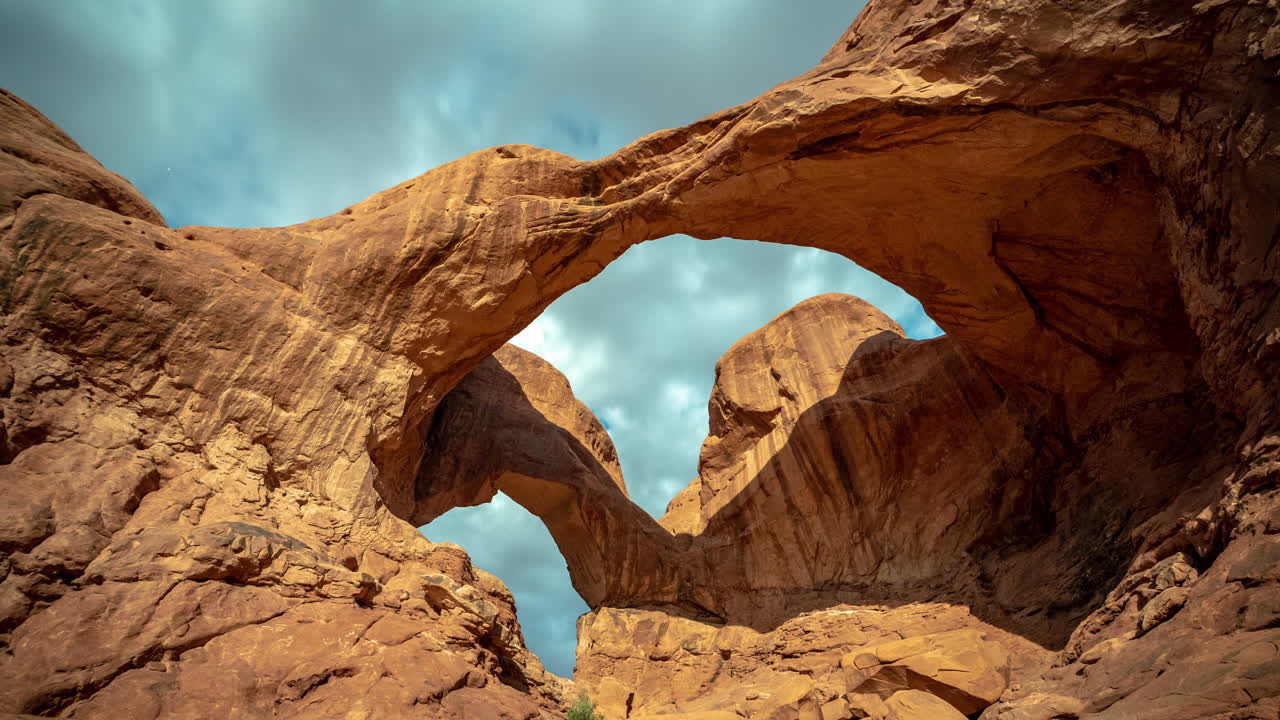 Selang Waktu Lengkungan Ganda Alami dan Langit Berawan Dinamis Dramatis di Atas Tengara Alam Taman Nasional Arches, Utah, AS