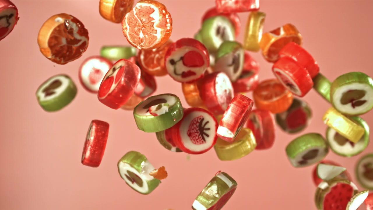 Bunte Fruchtbonbons fallen in Zeitlupe vor pinkem Hintergrund