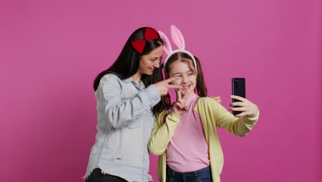 playful cheery mother and girl smiling for photos on smartphone