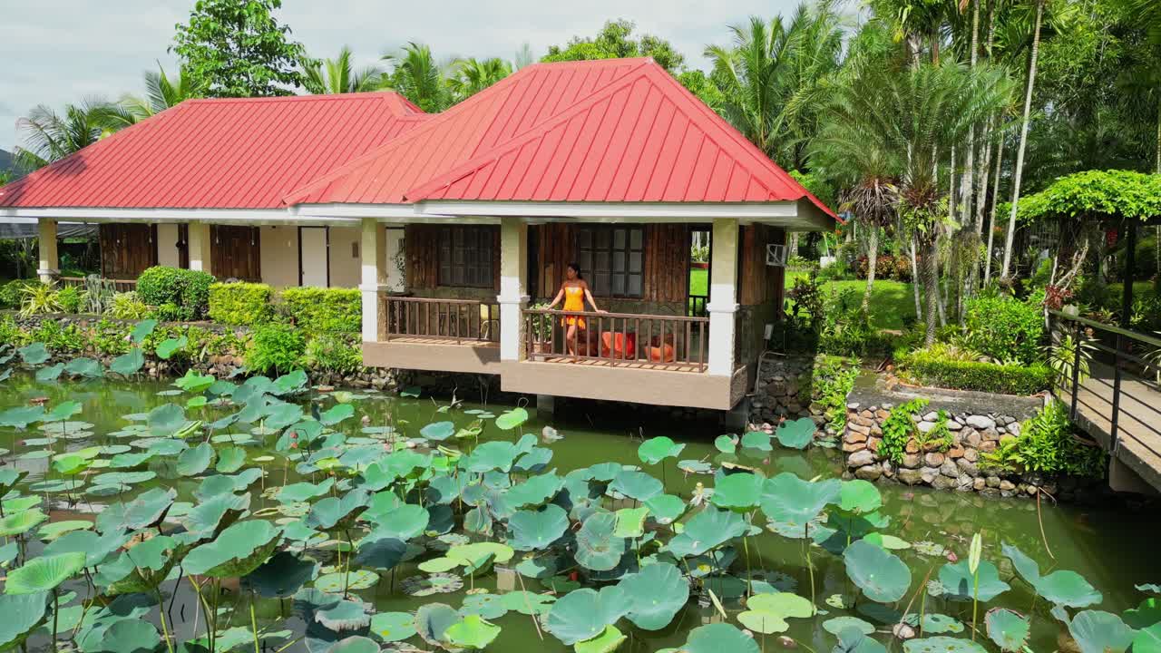 Một cú lia máy quay vòng tròn ghi lại cảnh một người phụ nữ đang đứng trên ban công nhà nổi nhìn ra những thảm lá sen dày đặc trên ao tại Khách sạn Palaisdaan, Nueva Vizcaya, Philippines