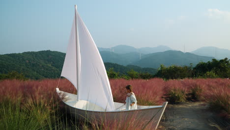 child playing inside wooden sail boat at pink muhly grass field - herb island farm in pocheon