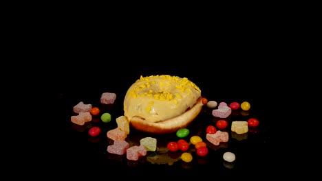 yellow funny surprised glazed donut with sprinkles, striped caramel candies, colorful dragee with raisins or peanuts inside rotate on black background