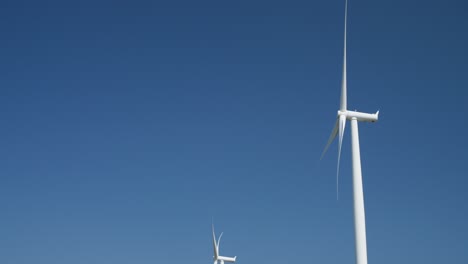 wind turbines spinning under clear blue sky with minimal cloud coverage. renewable energy sources generate clean electricity in vast open space. sustainable technology in action