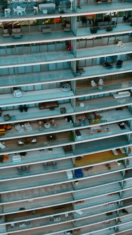 descending along the huge residential block of flats with spacious balconies. drone footage of a house in miami. top view. vertical video