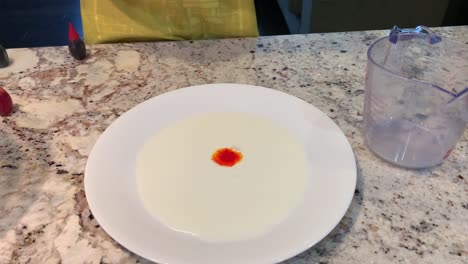 Small-hands-dropping-different-colors-of-food-coloring-onto-a-plate-of-white-milk