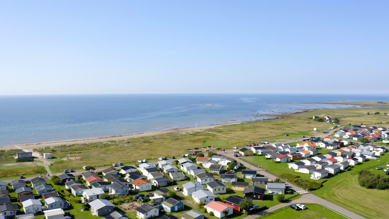 Flyvende over en landsby med små strandhytter ved stranden.