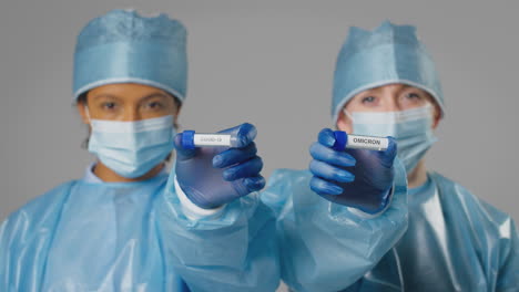 studio shot of female lab research workers in ppe holding test tubes labelled covid-19 and omicron