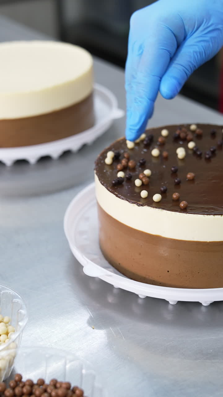 Chocolate, cocoa and milk dragee candies are put on top of the cake. Tasty cakes are decorated with little sweet peas. Close up. Vertical video