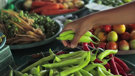 A-close-up-shot-of-a-girl-choosing-green-chilli-peppers-in-a-street-market-in-Thailand,-south-east-asia