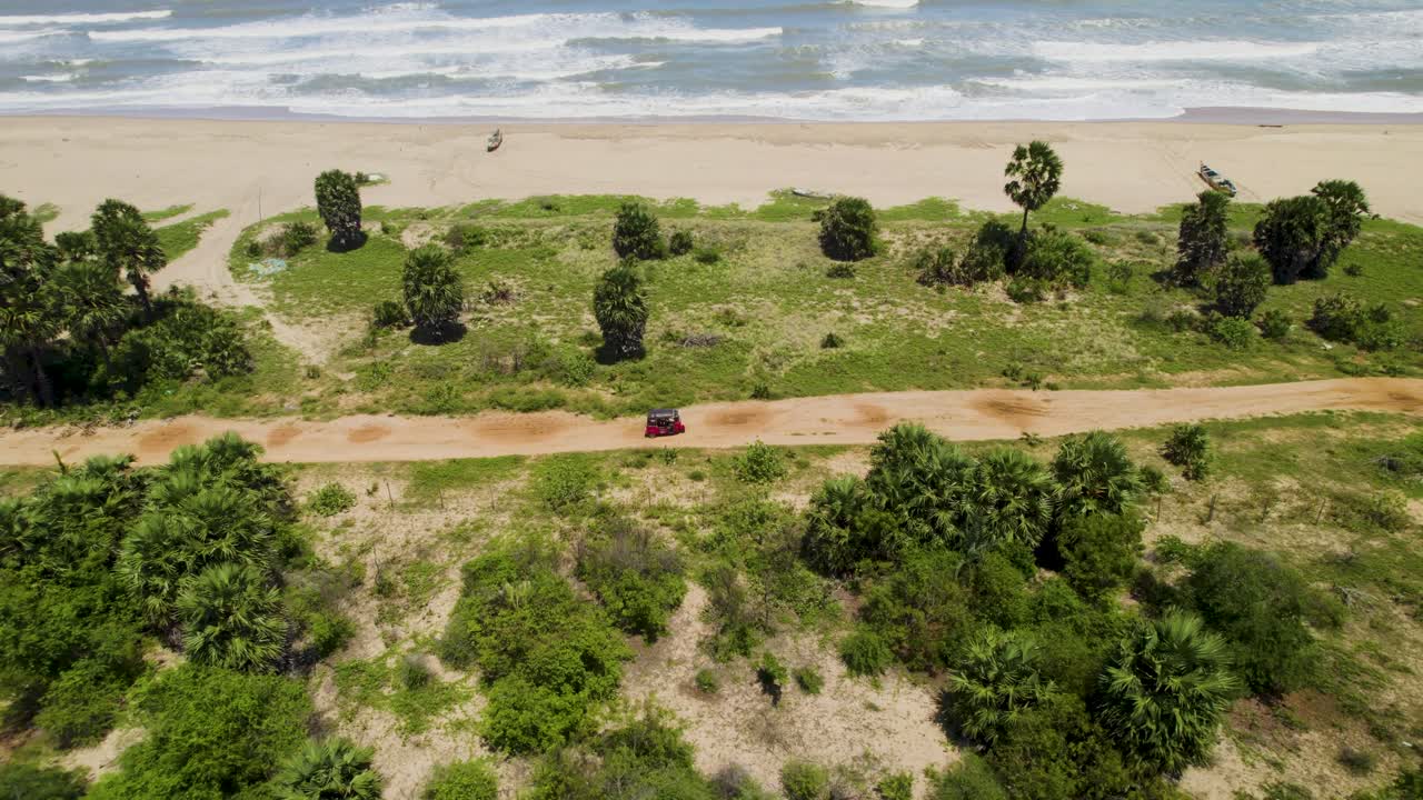 Aerial view of a car driving on a dirt road along a tropical coast