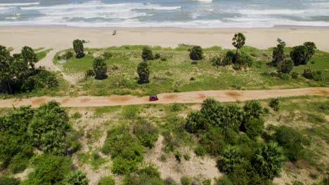 aerial view of a car driving on a dirt road along a tropical coast