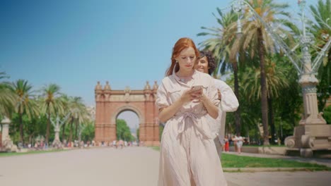 chica enfocada buscando teléfono móvil cerca del monumento. hombre sonriente cerrando los ojos de la mujer