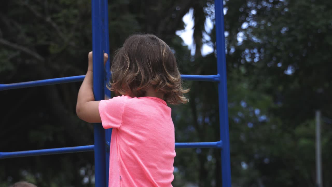 hermosa niña de cuatro años jugando en el gimnasio de la jungla con gran habilidad usando camiseta rosa y moviéndose de izquierda a derecha