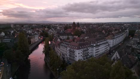 breathtaking aerial view of strasbourg at twilight, featuring a glowing canal, rows of classic european buildings, and distant cathedral towers beneath dramatic pink and purple sunset clouds