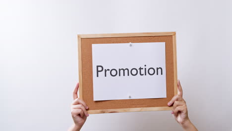 Woman's-hand-shows-the-paper-on-board-with-the-word-Promotion-in-white-studio-background-with-copy-space