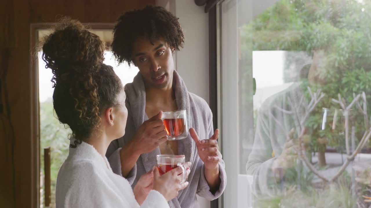 Video of relaxed diverse couple in bath robes drinking tea and talking at health spa