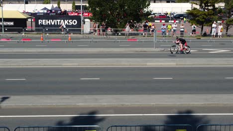 drone footage captures the tallinn triathlon event with participants on bikes and spectators watching from the sidelines on a sunny day