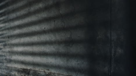 Medium-shot-of-grungy-concrete-wall-with-shadow-of-blinds-on-it-as-car-slowly-drives-by