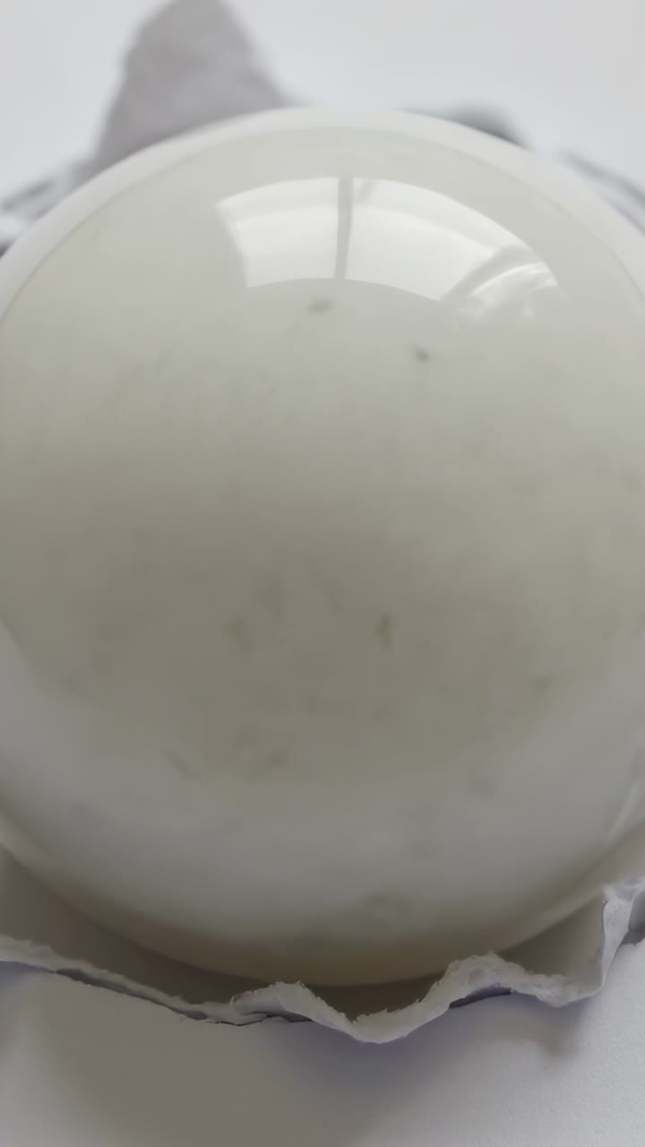 Vertical video: Shifting cam slightly, window light bathing peeled egg on shell fragments, gleaming