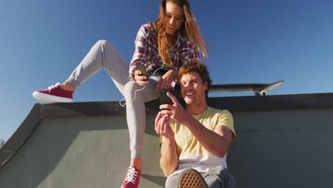 happy caucasian female and male friends using smartphone on sunny day