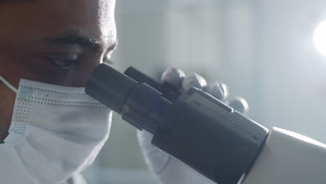 científico con máscara y guantes mirando a través del microscopio