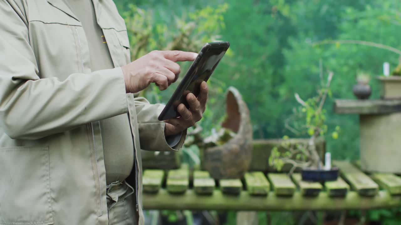 Midsection of caucasian male gardener using tablet at garden center