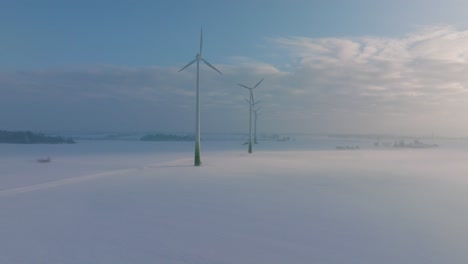 aerial establishing view of wind turbines generating renewable energy in the wind farm, snow filled countryside landscape with fog, sunny winter day, wide ascending drone shot moving forward