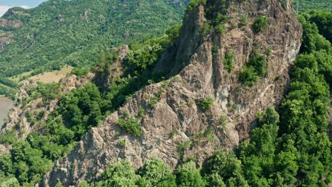 Lush-greenery-covers-the-rugged-Pietrele-Rosiei-peak-under-a-clear-sky,-aerial-view