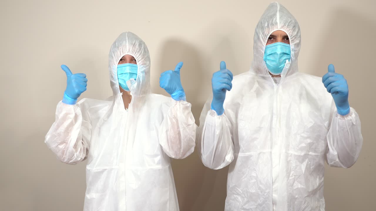 doctors dressed in ppe suits drawing a smile with their hands and thumbs up