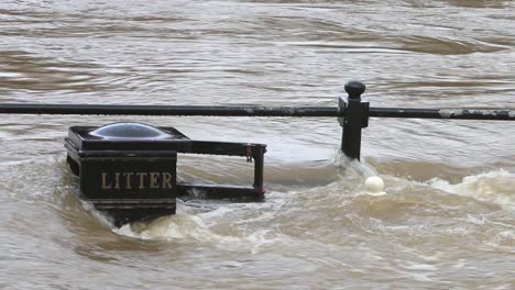 el río severn durante una inundación de invierno que fluye sobre barandillas y un contenedor de basura