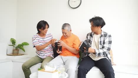 elderly asian father and teen sons talking and holding virtual reality headsets at home