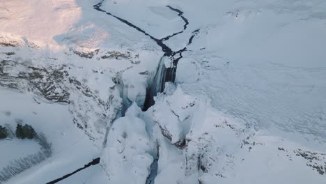 aerial view of a winter landscape covered in snow, over skogafoss waterfall, in iceland, at sunset