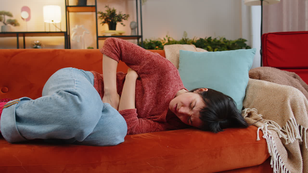 Upset woman embracing belly suffering from stomachache menstrual painful feelings lying on sofa