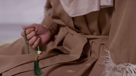 close up of muslim woman wearing hijab praying at home with prayer beads