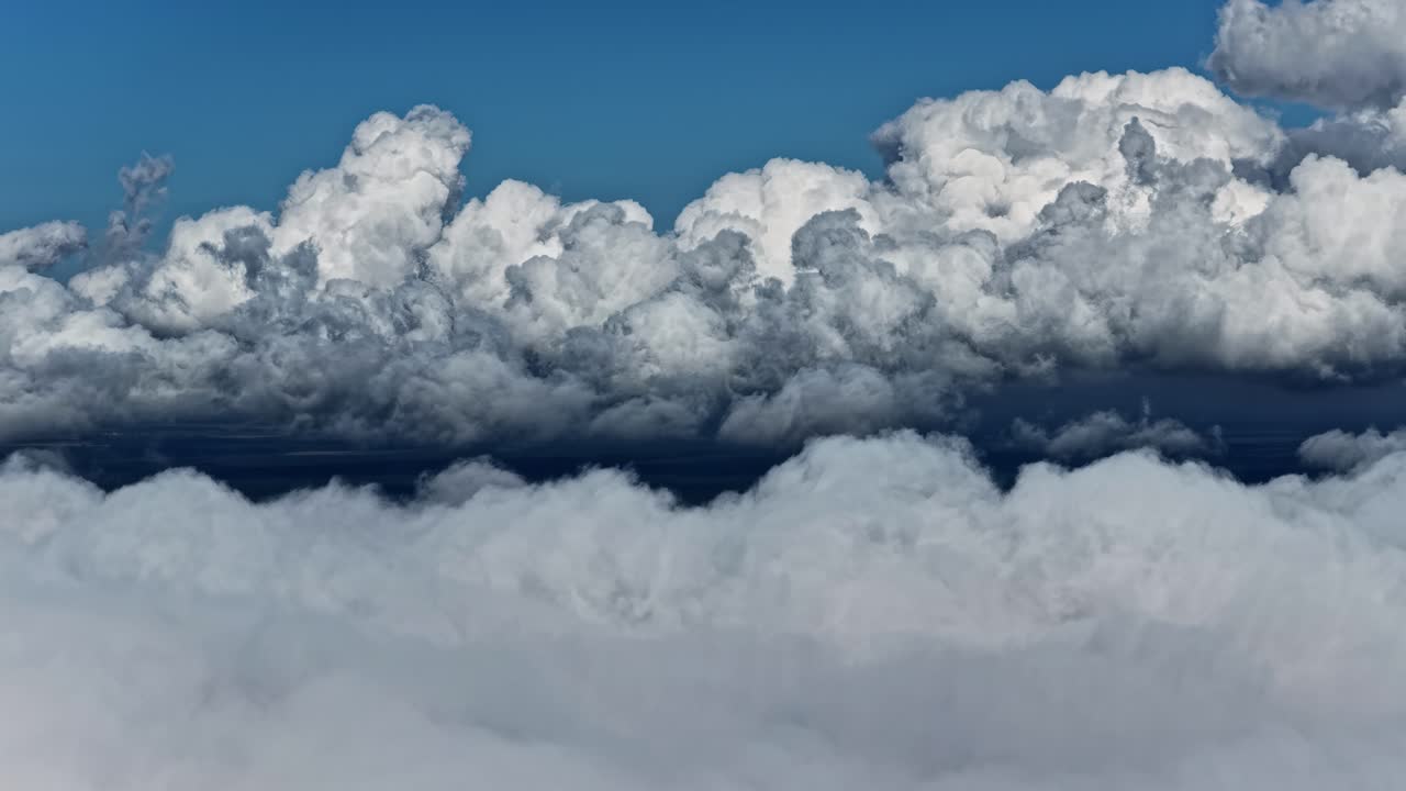 Towering white clouds rise above a bright sky as the camera ascends smoothly, revealing dramatic cloud formations and crisp blue atmosphere