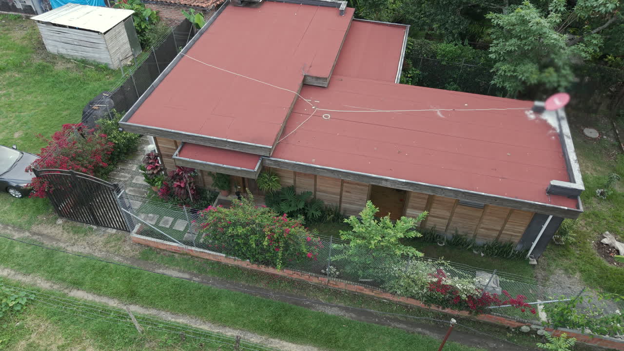 Drone video of a charming rustic home surrounded by lush greenery in Valle del Cauca, Colombia. Captured from above, highlighting beautiful gardens and vibrant red roof under cloudy skies