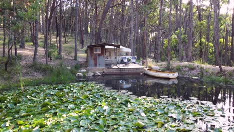 A-wide-rotating-drone-shot-of-a-beautiful-tiny-home-on-a-lake-in-a-forest