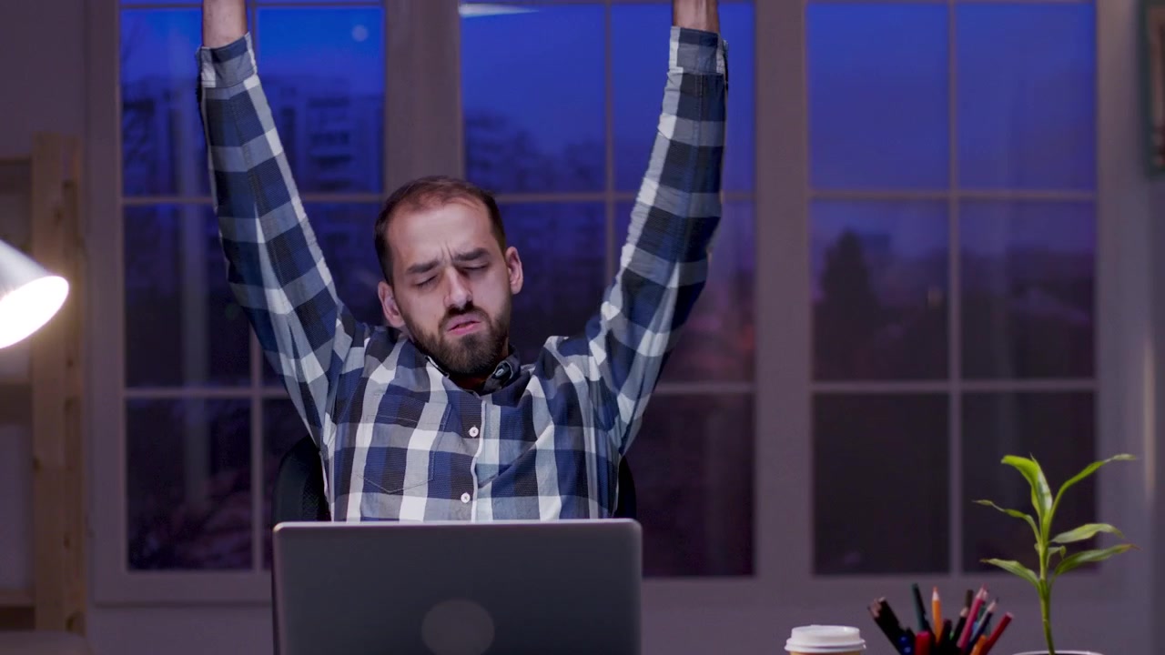 Uomo stanco che si stira alla scrivania mentre lavora fino a tardi al computer portatile
