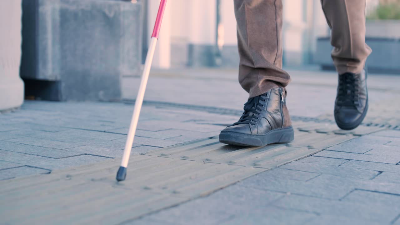 persona ciega usando bastón blanco en azulejos táctiles rectos para navegar por la carretera