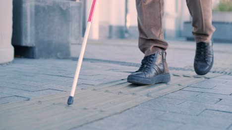 persona ciega usando bastón blanco en azulejos táctiles rectos para navegar por la carretera