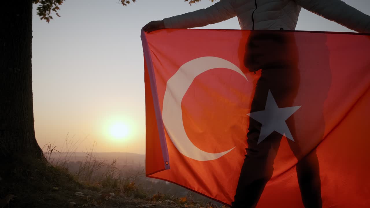 Gün batımında dışarıda duran, Türk bayraklı mutlu kadının arkadan geniş çekimi.